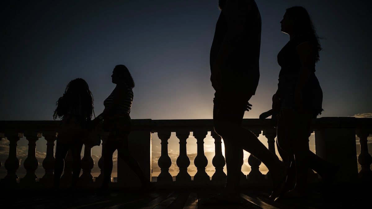 Silhouettes of people walking by a railing at dusk.